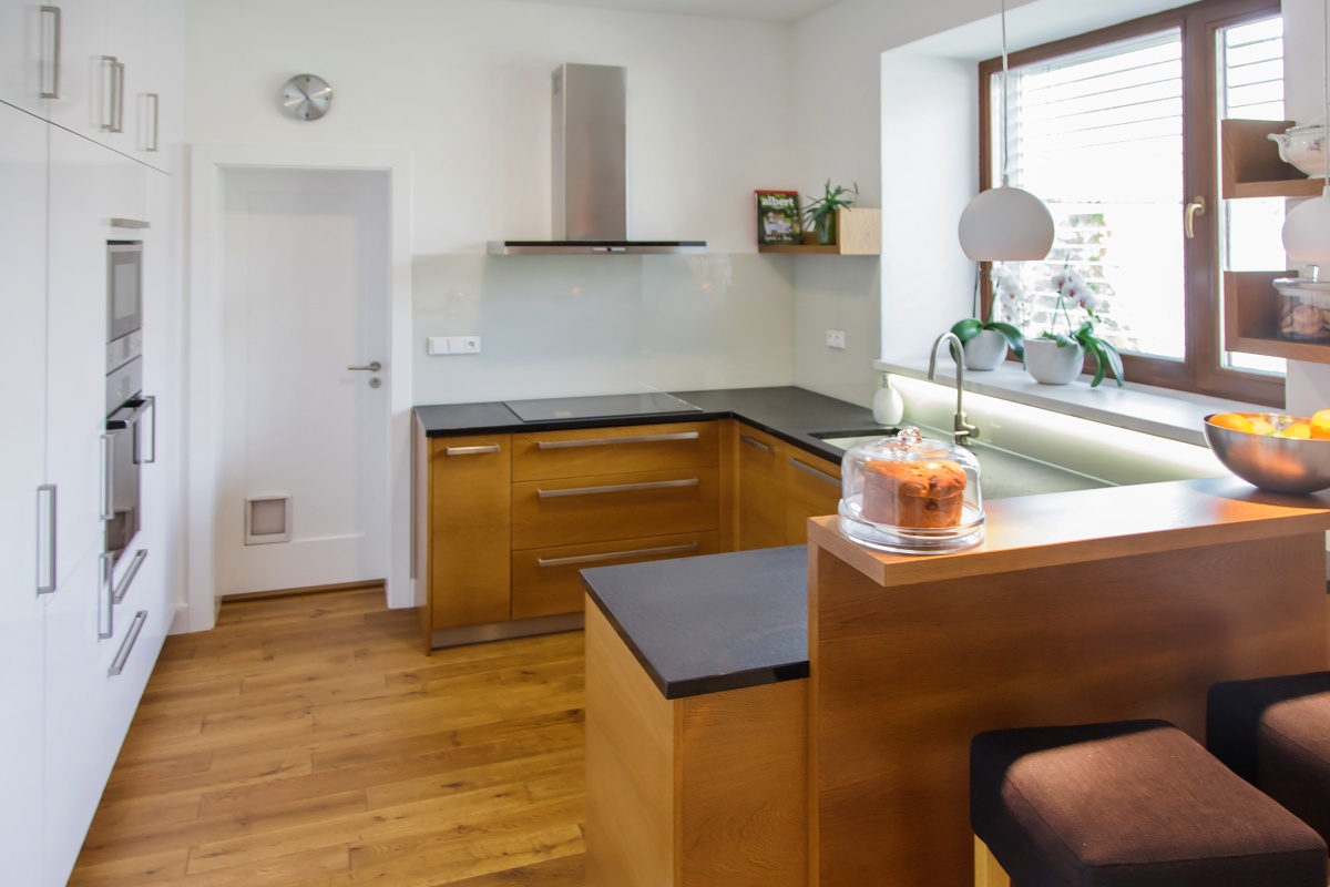 Family house  - The kitchen is divided in two separate parts. For the purposes of maintaining the lightness of the area, the roomy storage space – a system of fitted cabinets – is made from high-gloss white laminate. Apart from an oven and microwave, it also contains a fridge and freezer. The second part of the kitchen is made from varnished oak veneer. The worktop is granite and has an incredibly practical under-mount sink. The facing behind the worktop is made from the Lacomat glass.