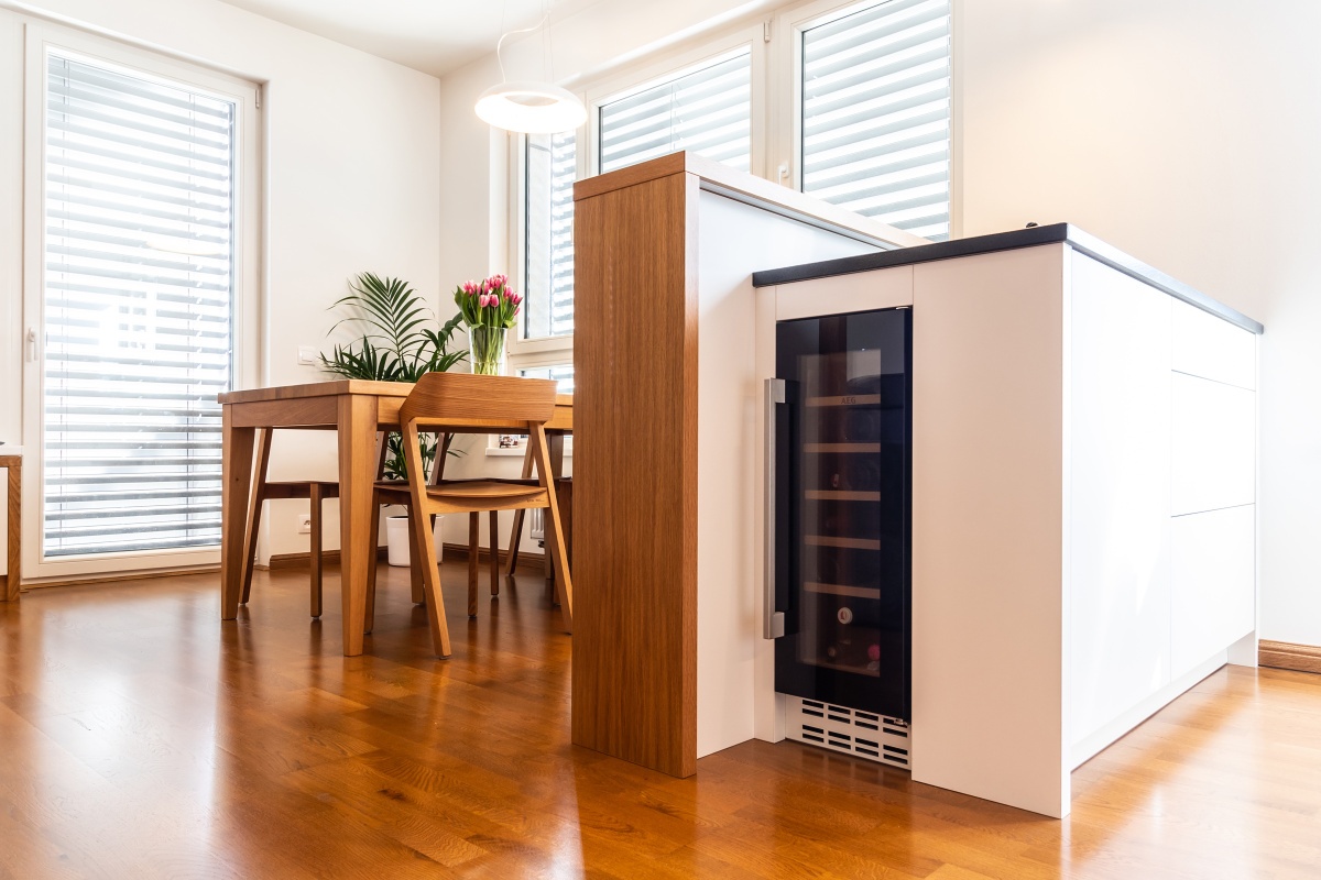 Interior of Apartment in New Building - The kitchen is finished with white laminated particle board in deep matte and oak veneer. The worktop surface is granite; the island under the worktop conceals a wine rack. The tiered top cabinets in the kitchen allow storage spaces to be used right up to the ceiling. All doors are operable by means of the handle-free tip-on system. The waste bin is fitted with an electric Servo-Drive.